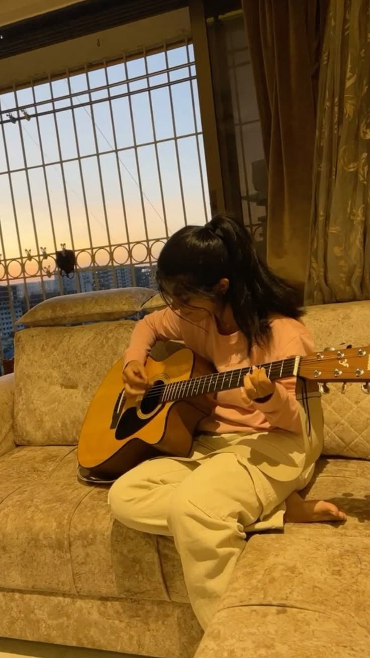 A musician playing acoustic guitar on a sofa at sunset